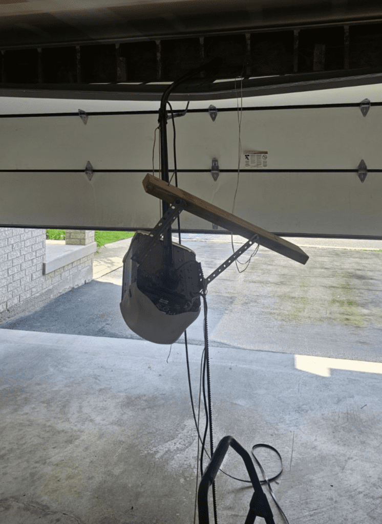 Damaged garage door opener hanging after falling from ceiling, in need of repair.